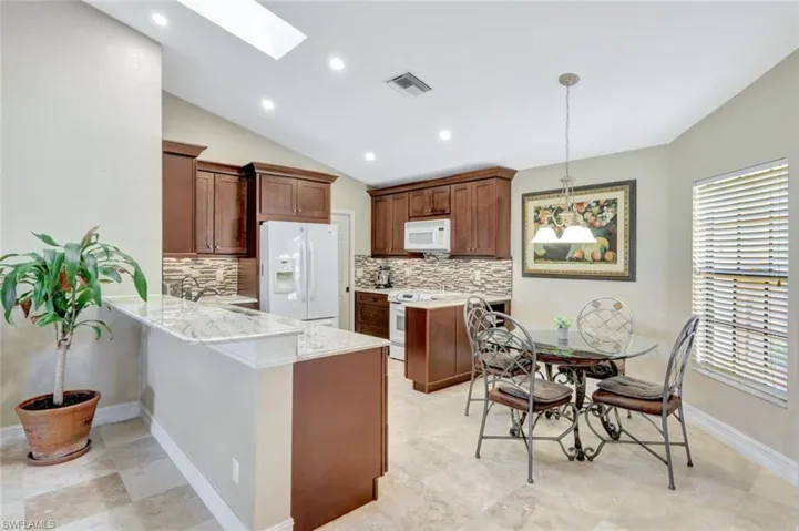 Kitchen with lofted ceiling with skylight, pendant lighting, decorative backsplash, kitchen peninsula, and white appliances