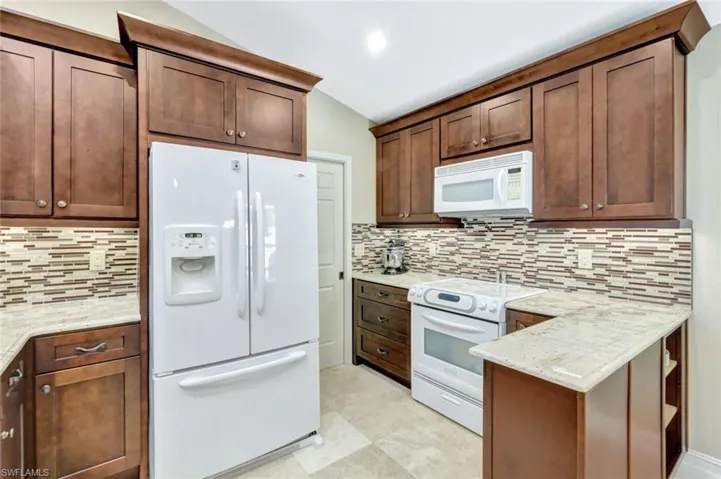 Kitchen featuring tasteful backsplash, light stone countertops, and white appliances