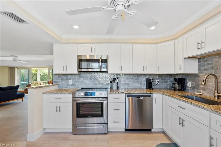 Kitchen featuring subway tile  backsplash, granite countertops, white cabinets, and stainless steel appliances.