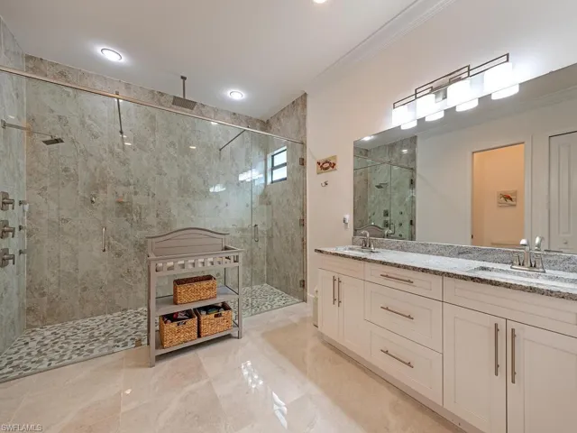 Full bath with ornamental molding, a shower stall, double vanity, and marble finish floors