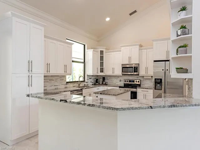 Kitchen with stainless steel appliances, open shelves, a sink, light stone countertops, and decorative backsplash