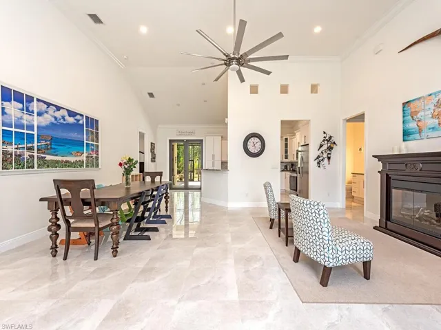 Dining room with baseboards, a ceiling fan, ornamental molding, high vaulted ceiling, and a glass covered fireplace
