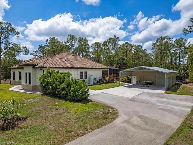 View of side of home featuring stucco siding, a tile roof, asphalt driveway, a yard, and a detached carport