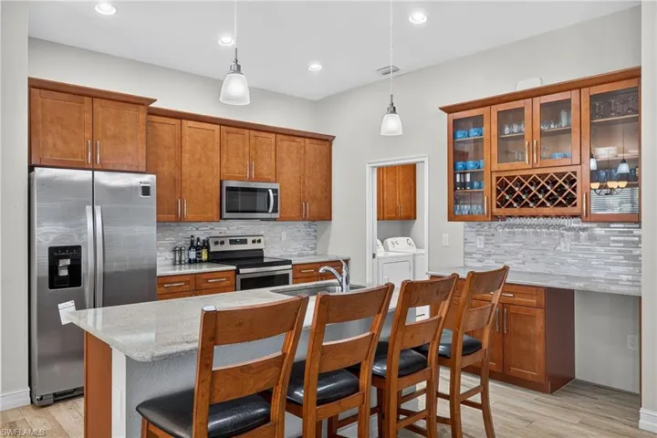 Kitchen featuring a central island with countertop seating, stainless steel appliances, wood-finish cabinetry, and a tile backsplash