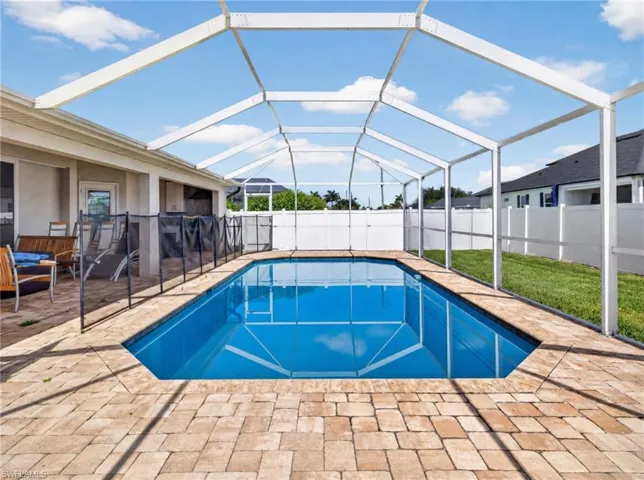 Screened outdoor swimming pool with paver decking, a safety fence, and a white privacy fence