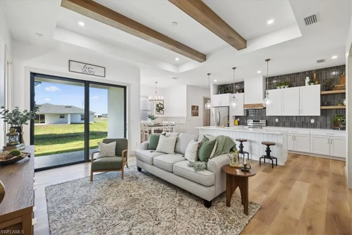 Living room with beamed ceiling, a tray ceiling, light wood-type flooring, and a chandelier