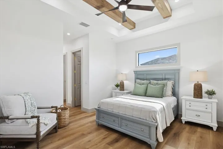 Bedroom featuring beam ceiling, ceiling fan, hardwood / wood-style flooring, and a raised ceiling