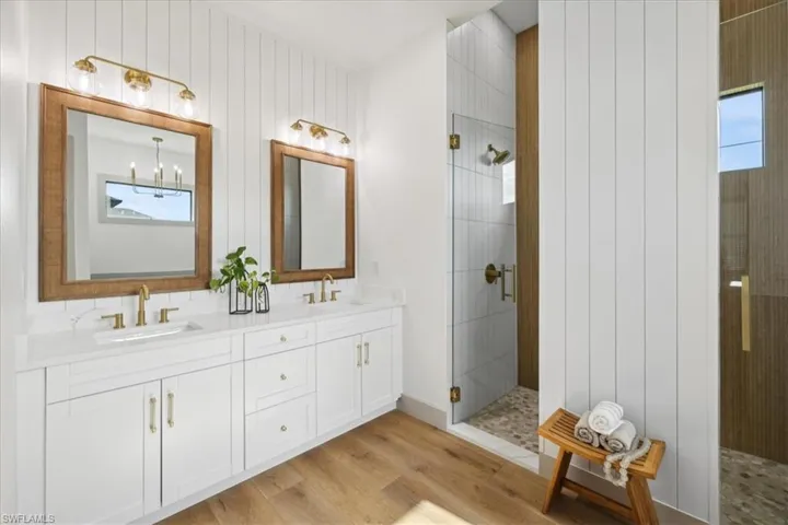 Bathroom featuring dual vanity, a notable chandelier, tiled shower, and hardwood / wood-style floors