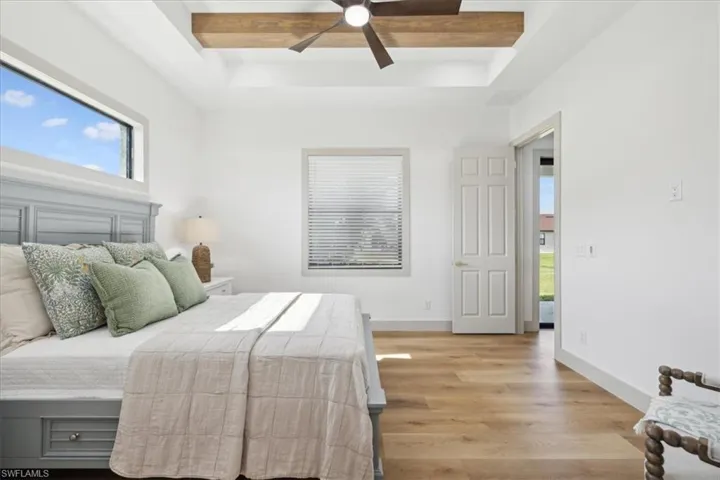 Bedroom with a raised ceiling, beamed ceiling, ceiling fan, and light wood-type flooring