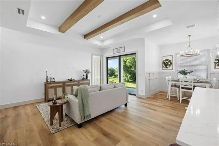 Living room featuring beam ceiling, a chandelier, a raised ceiling, and light hardwood / wood-style flooring