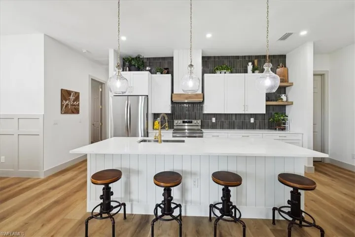 Kitchen with light hardwood / wood-style floors, pendant lighting, sink, white cabinetry, and appliances with stainless steel finishes