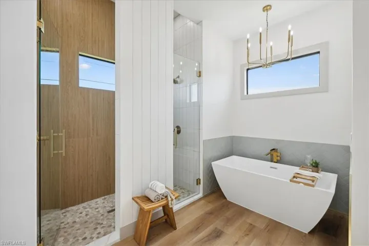 Bathroom with a wealth of natural light, hardwood / wood-style floors, separate shower and tub, and a chandelier