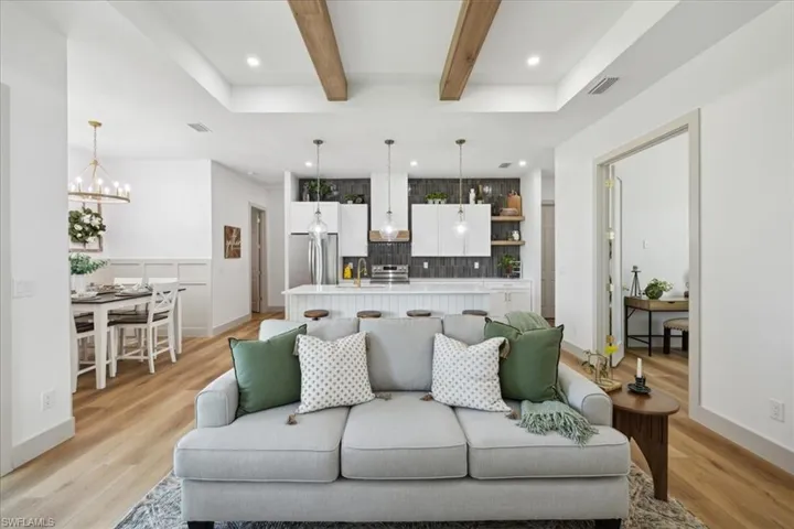 Living room with beamed ceiling, sink, light hardwood / wood-style flooring, and an inviting chandelier