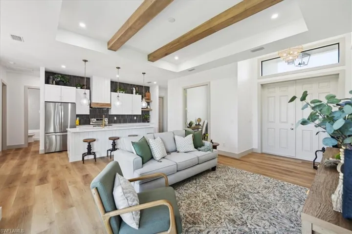 Living room with an inviting chandelier, beam ceiling, light hardwood / wood-style flooring, and a raised ceiling