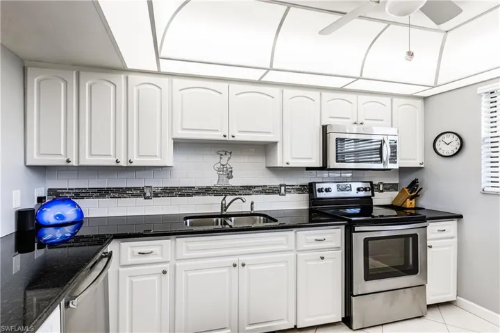 Kitchen featuring appliances with stainless steel finishes, white cabinets, dark stone counters, and ceiling fan