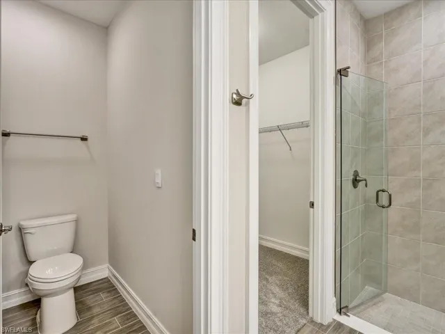 Bathroom featuring a walk in closet, a stall shower, and wood finish floors