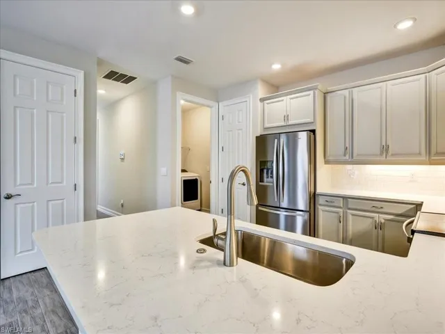 Kitchen featuring stainless steel fridge, light stone counters, recessed lighting, backsplash, and gray cabinets