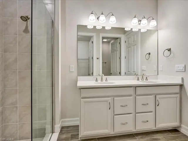 Bathroom featuring double vanity, tiled shower, and wood tiled floors
