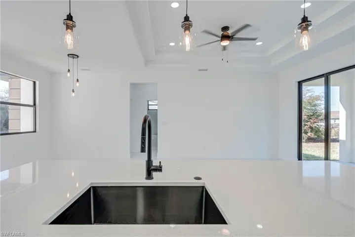 Kitchen with healthy amount of natural light, pendant lighting, light stone counters, and ceiling fan