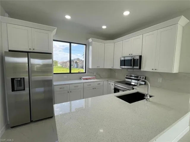 Kitchen with stainless steel appliances, white cabinets, light stone countertops, kitchen peninsula, and backsplash
