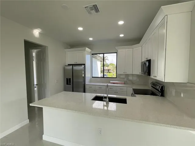 Kitchen with stainless steel refrigerator with ice dispenser, sink, range with electric stovetop, light stone countertops, and kitchen peninsula