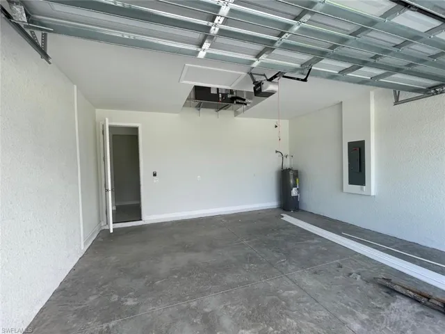 Garage with water heater, electric panel, and a garage door opener
