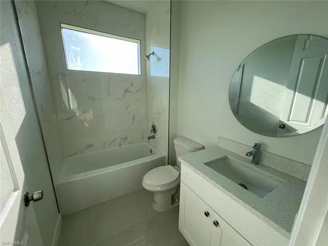 Full bathroom with vanity, tiled shower / bath combo, toilet, and tile patterned floors