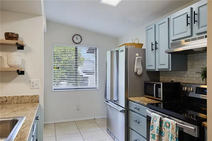 Kitchen with appliances with stainless steel finishes, under cabinet range hood, backsplash, light tile patterned floors, and lofted ceiling