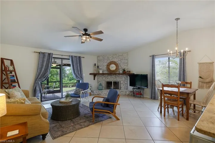 Living room with a chandelier, ceiling fan, light tile patterned floors, a stone fireplace, and vaulted ceiling
