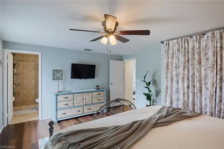 Bedroom featuring dark wood-style floors, ensuite bath, and a ceiling fan
