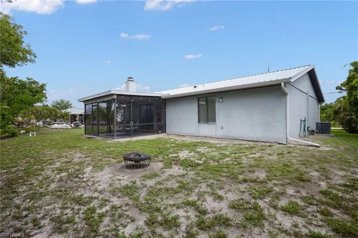 Back of house with a sunroom, a fire pit, stucco siding, a chimney, and a metal roof
