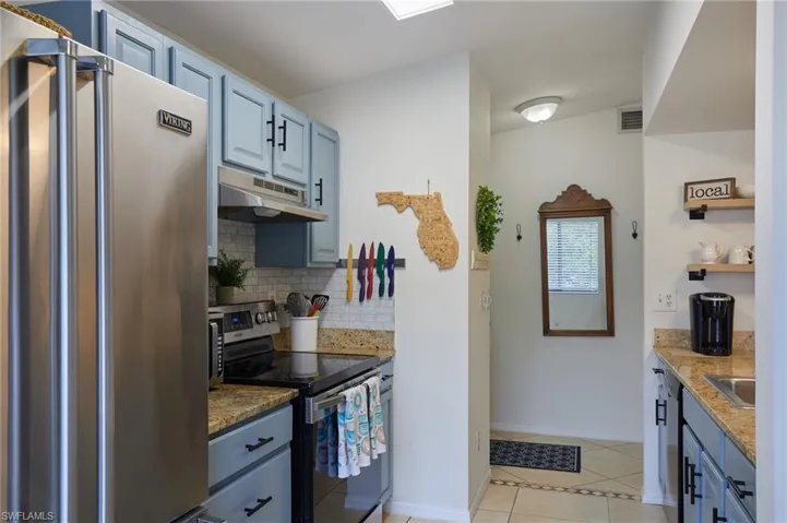 Kitchen with appliances with stainless steel finishes, under cabinet range hood, backsplash, blue cabinetry, and light tile patterned floors