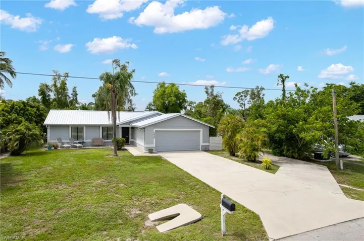 Ranch-style home with a garage, driveway, a front yard, and a metal roof