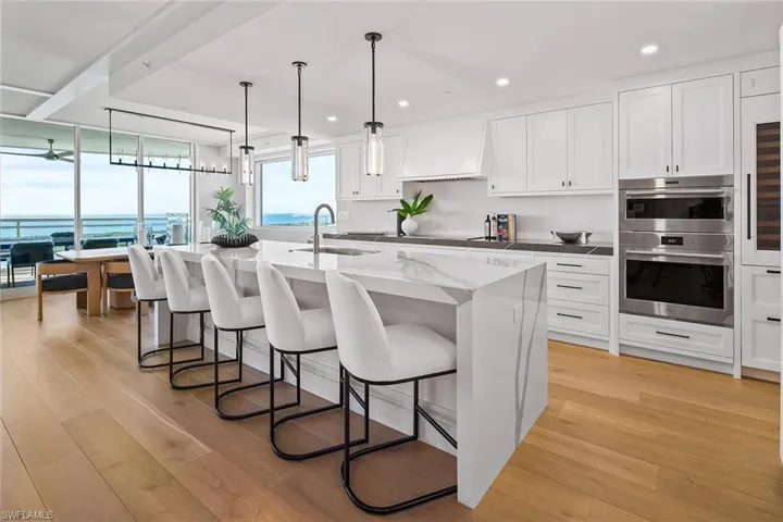 The chef's kitchen features Wolf and Sub-Zero appliances, quartz countertops, oversized island, wine cooler, refrigerator and freezer drawers, with water views just beyond
