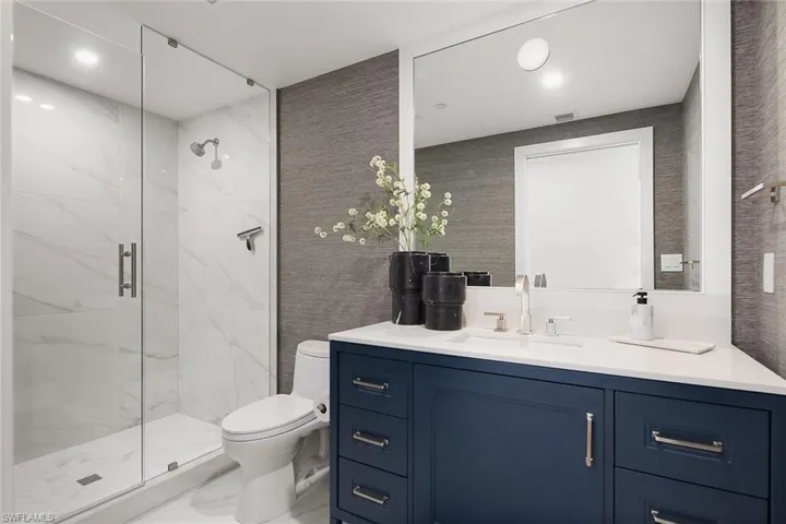 Third guest en-suite bath featuring a glass walk-in shower, quartz surfaces, custom cabinetry, and designer wallpaper.