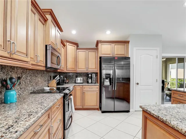 Kitchen featuring backsplash, appliances with stainless steel finishes, light stone countertops, and light tile flooring