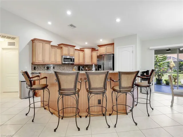 Kitchen with a breakfast bar area, appliances with stainless steel finishes, tasteful backsplash, and light tile floors