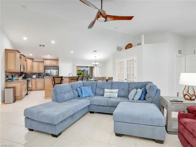 Tiled living room featuring vaulted ceiling and ceiling fan with notable chandelier