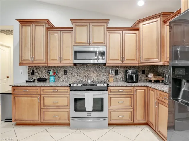 Kitchen featuring stainless steel appliances, light stone countertops, tasteful backsplash, and light tile floors