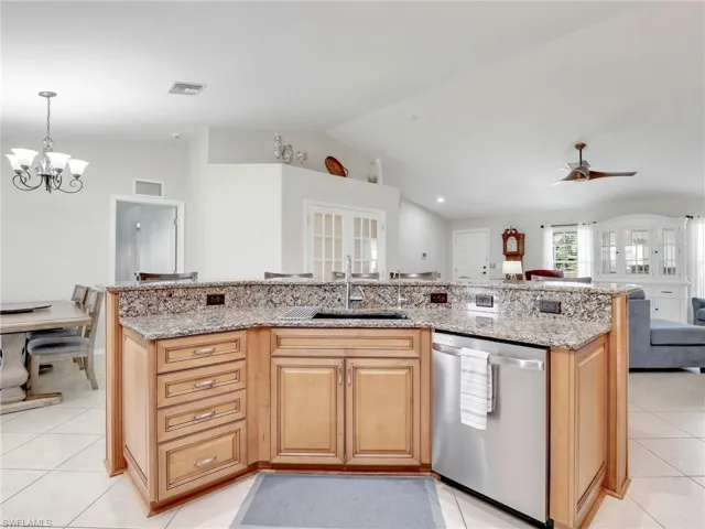 Kitchen with dishwasher, sink, light stone counters, and ceiling fan with notable chandelier