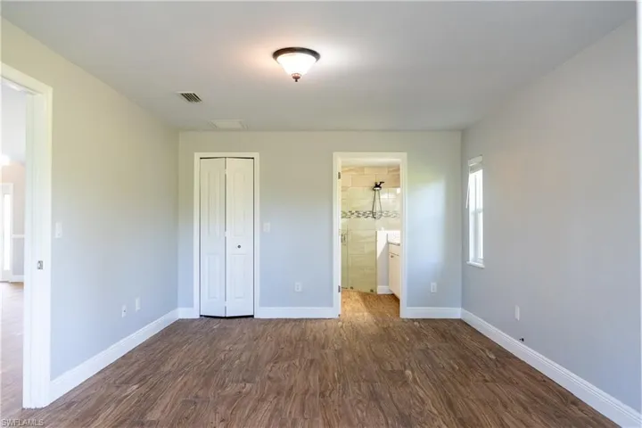 Unfurnished bedroom featuring dark wood finished floors, a closet, and ensuite bath