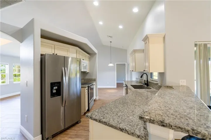 Kitchen with appliances with stainless steel finishes, light stone counters, hanging light fixtures, cream cabinetry, and light wood-type flooring