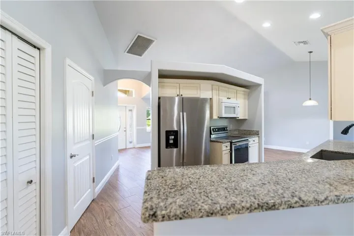 Kitchen featuring arched walkways, appliances with stainless steel finishes, light stone counters, light wood finished floors, and pendant lighting