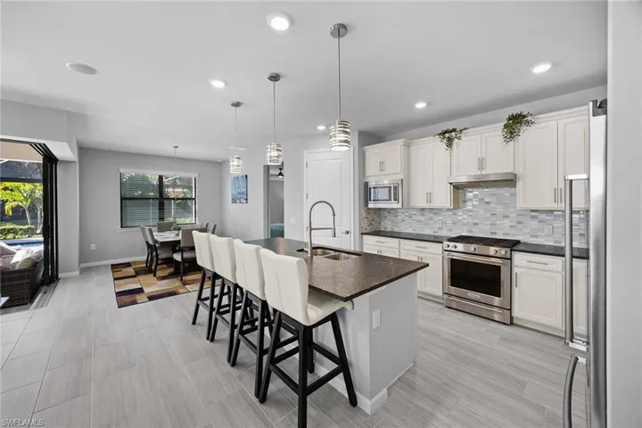 Kitchen featuring appliances with stainless steel finishes, a kitchen island with sink, decorative light fixtures, a breakfast bar, and decorative backsplash