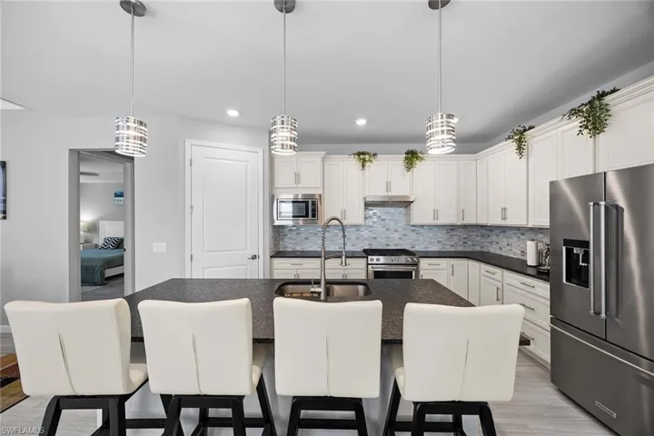 Kitchen with high quality appliances, a kitchen bar, an island with sink, white cabinetry, and recessed lighting