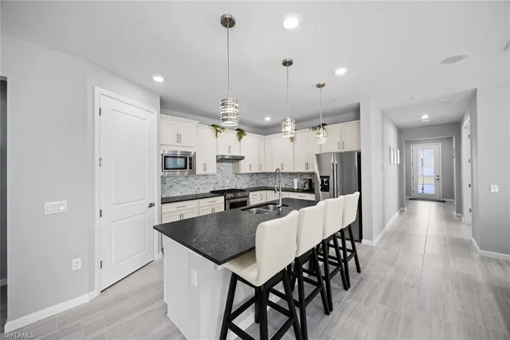 Kitchen featuring a breakfast bar area, a center island with sink, hanging light fixtures, high end appliances, and recessed lighting