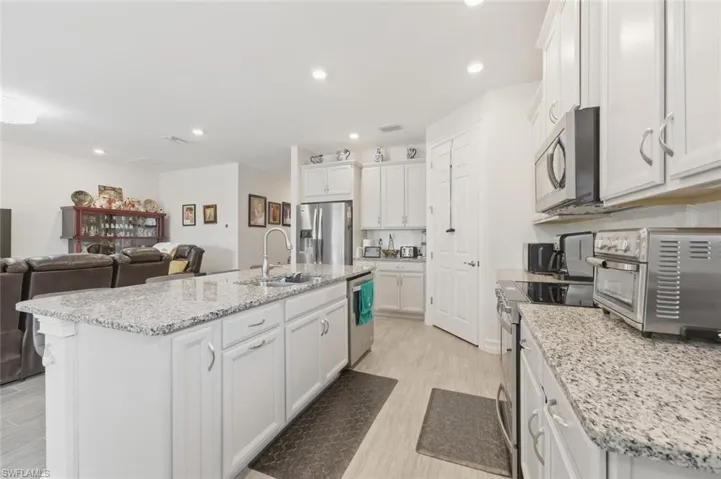 Kitchen featuring light stone countertops, stainless steel appliances, white cabinets, a center island with sink, and open floor plan