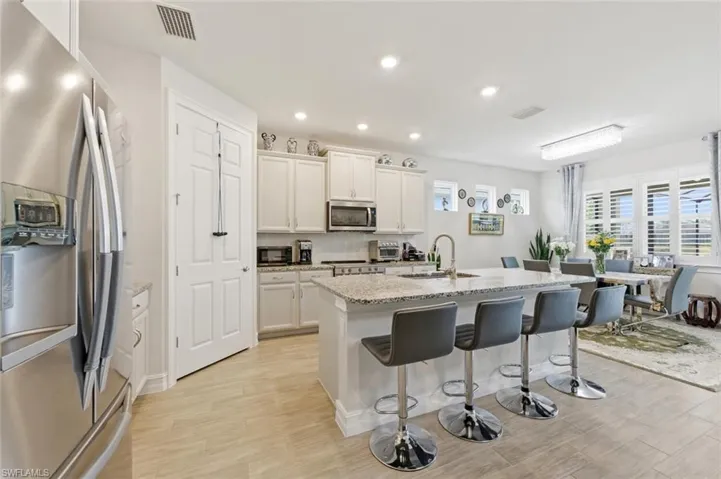 Kitchen featuring stainless steel appliances, a breakfast bar area, an island with sink, light stone counters, and white cabinetry