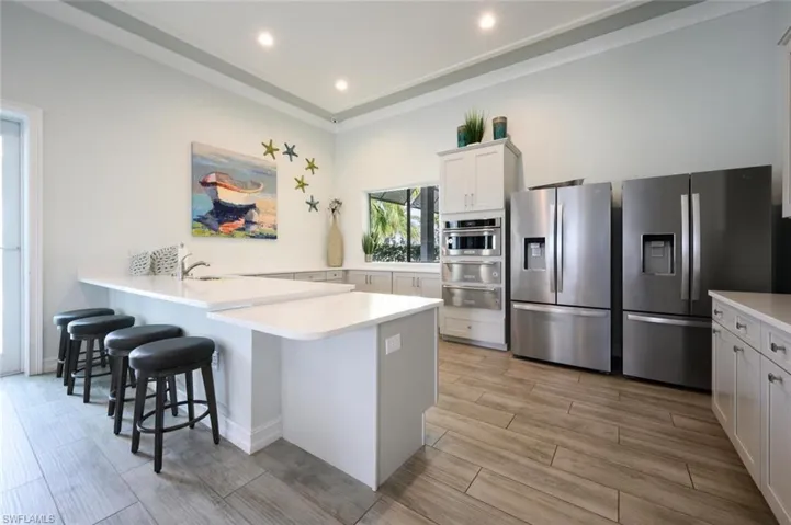 Kitchen with stainless steel fridge, a breakfast bar area, wood tiled floors, a peninsula, and recessed lighting