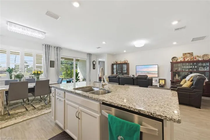Kitchen featuring stainless steel dishwasher, open floor plan, light wood-style flooring, light stone counters, and recessed lighting
